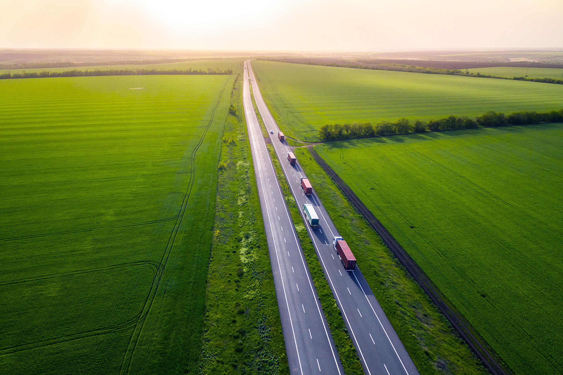 trucks on the higthway sunset. cargo delivery driving on asphalt road along the green fields. seen from the air. Aerial view landscape. 