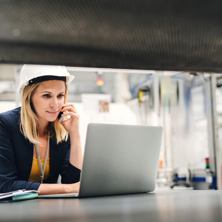 Industrial woman engineer in a factory using laptop and smartphone.