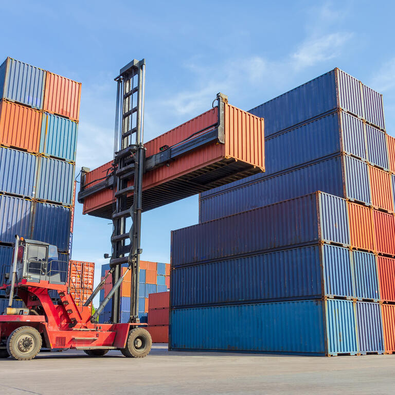 Forklift handling container box loading to truck in shipping yard with cargo container background.