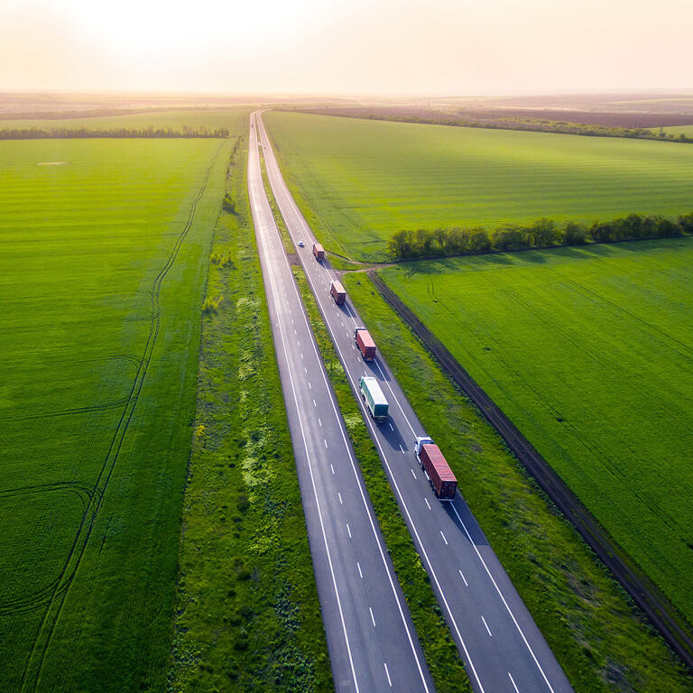 trucks on the higthway sunset. cargo delivery driving on asphalt road along the green fields. seen from the air. Aerial view landscape. 