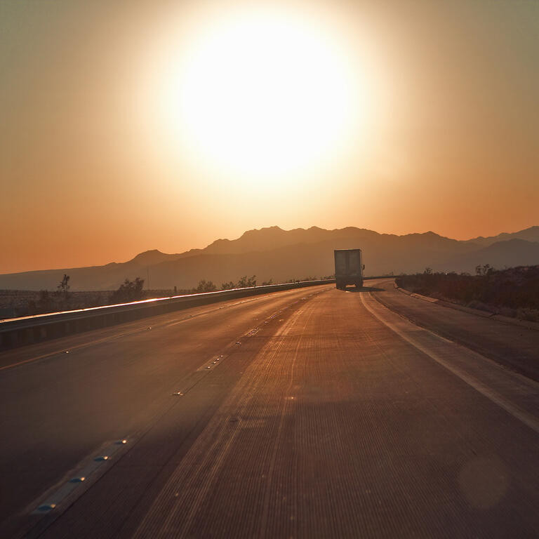 18-wheeler semi-trucks at sunset hit the highway driving down Interstate Highway 15 between Los Angeles and Las Vegas Nevada.